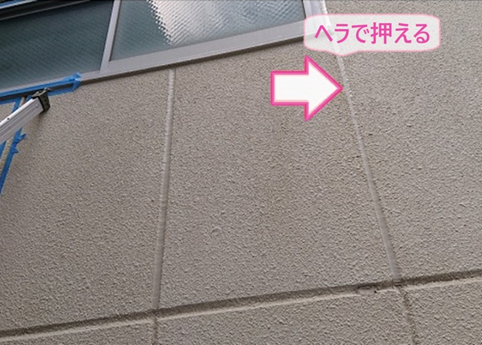 工場建屋の開口部の水漏れ補修でシーリングをヘラで押えて養生を撤去している様子