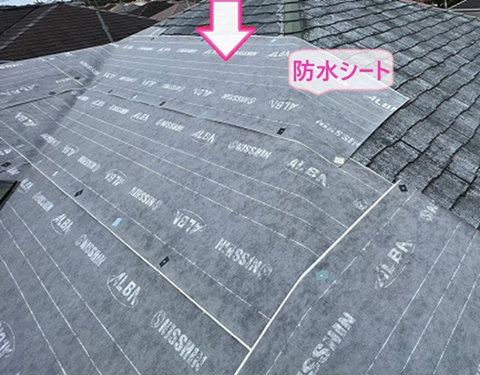 トップライトのあるスレート屋根の金属重ね張りで防水シートを貼っている様子