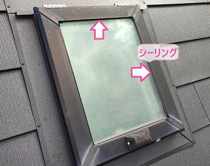スレート屋根の金属重ね張りでトップライトのガラスまわりにシーリングを打設している様子