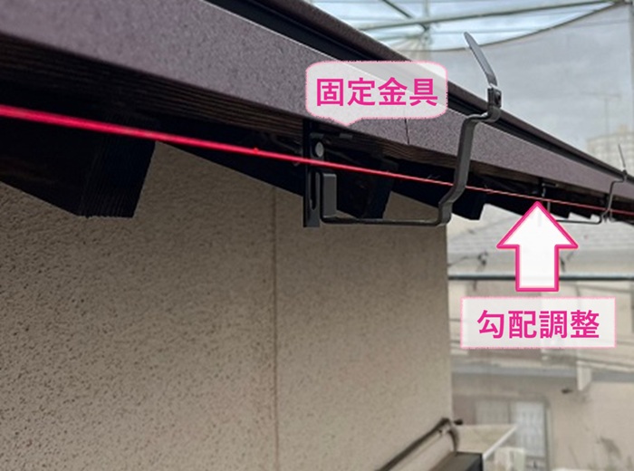 劣化した軒樋の取り替えで新しい固定金具を取り付けて勾配調整をしている様子