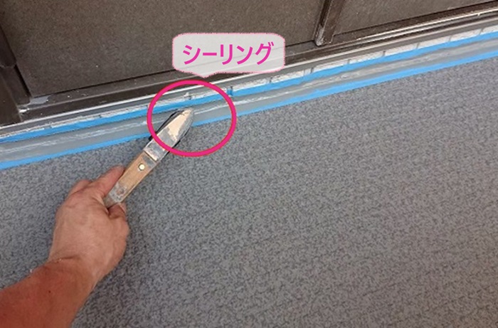 外部廊下と階段のリフォームで長尺シートの端部にシーリングを打っている様子