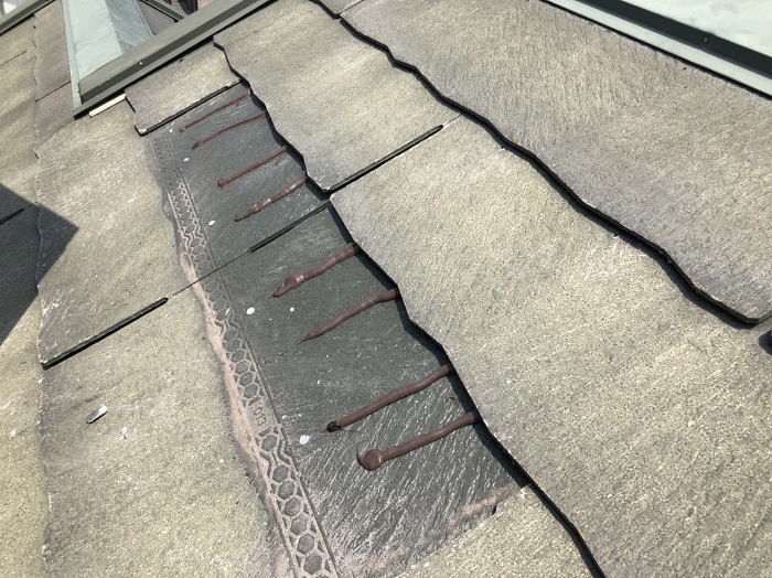 スレート屋根の差し替え補修工事で接着剤としてコーキングを塗っている様子