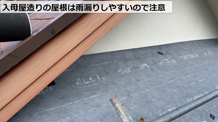入母屋造りのスレート屋根に防水シートを貼っている様子