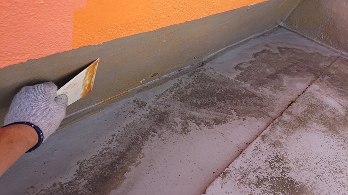 屋上の防水工事で立ち上がりに接着剤を塗っている様子
