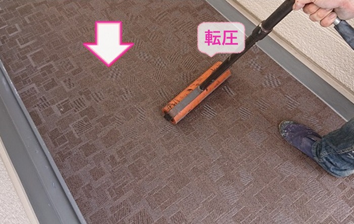 集合住宅の外階段メンテナンスで廊下に長尺シートを貼って転圧している様子