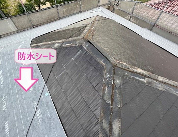 トップライトのあるスレート屋根の金属重ね張りで防水シートを貼っている様子