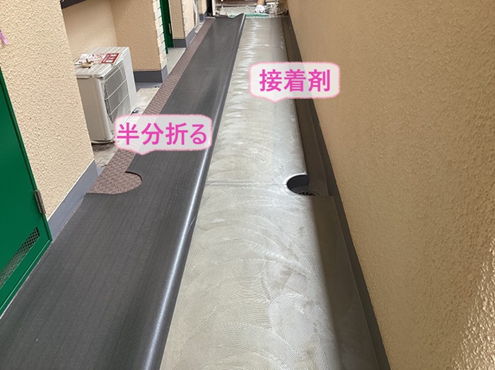 神戸市垂水区の階段廊下のリノベーションで集合住宅の廊下の側面に長尺シートを貼っている様子